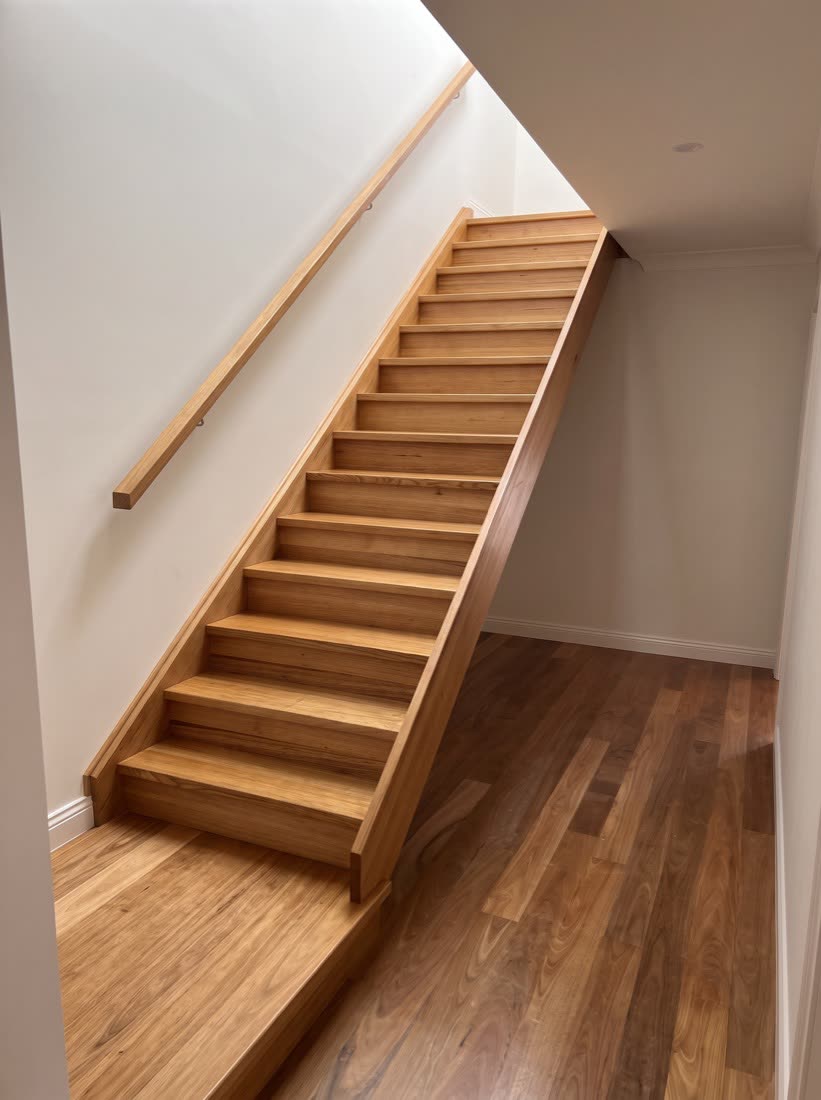 A straight flight of timber stairs with a timber handrail mounted on the wall